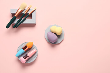 Decorative podiums with makeup sponges and brushes on pink background