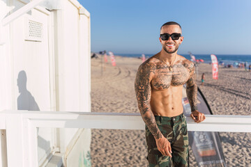 Chico joven tatuado y musculoso posando en verano en playa soleada