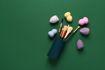 Makeup sponges and brushes on green background