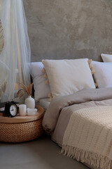Cozy bedroom with pillows, knitted beige plaid, candles and an alarm clock