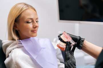 Close-up cropped shot of unrecognizable female dentist in protective mask and gloves showing jaw...