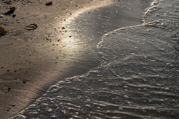 Soft ocean wave on sandy beach on sunset time, selective focus, textured pattern