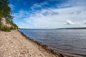 Obraz premium The bank of a large river with trees on the background of a blue sky with clouds in summer