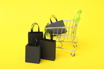 Shopping cart with bags on yellow background, closeup. Black Friday concept