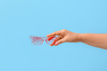 Woman holding stylish sunglasses on blue background