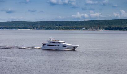 Yacht on a big river on the background of the shore with trees and blue sky with clouds in summer