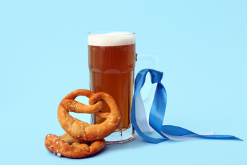 Mug of cold beer and tasty pretzels on blue background. Oktoberfest celebration