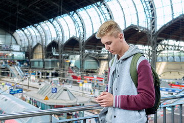 Young guy using mobile apps on smartphone standing at railway station
