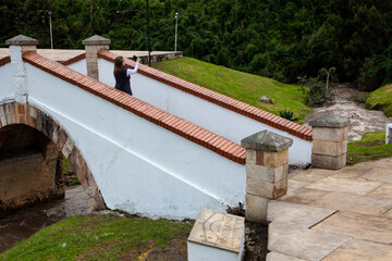 Female tourist taking selfies at the famous historic Bridge of Boyaca in Colombia. The Colombian independence Battle of Boyaca took place here on August 7, 1819.