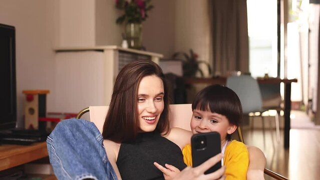 Happy mum have fun with son using smartphone apps at home, smiling mother hug preschool child boy having fun looking at cellphone relax with technology gadget, make video call, selfie. Selective focus