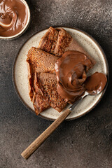 Chocolate crepes with chocolate paste on brown textured background rustic style top view, flat lay