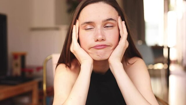 A displeased young woman rolls her eyes sitting at home in living room. Caucasian lady in displeasure, she is tired of situation, thinks how cant you still not understand, hold her head.