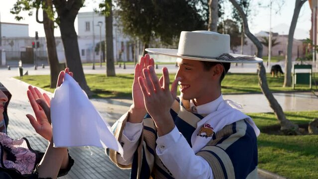 adult male dressed as a huaso clapping with his cueca dance partner in the square