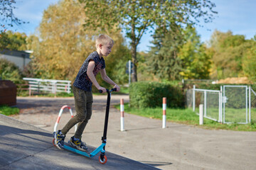 Child on kick scooter in park. Kids learn to skate roller board. Little boy skating on sunny summer day. Outdoor activity for children on safe residential street. Active sport for preschool kid. boy