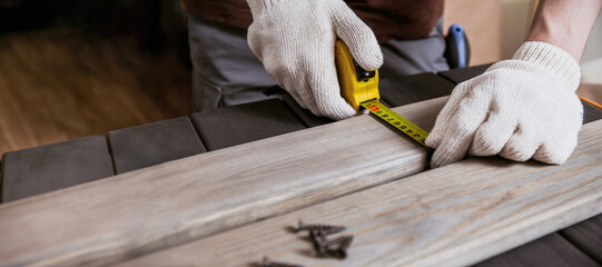 Exact measured. Close up of young male carpenter in gloves making measurements on the wooden plank by yellow measure tape