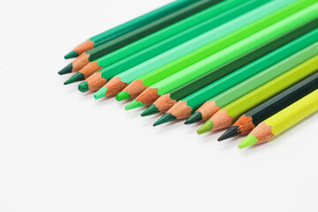 Multi-colored pencils lie on a white table, the green range of colors