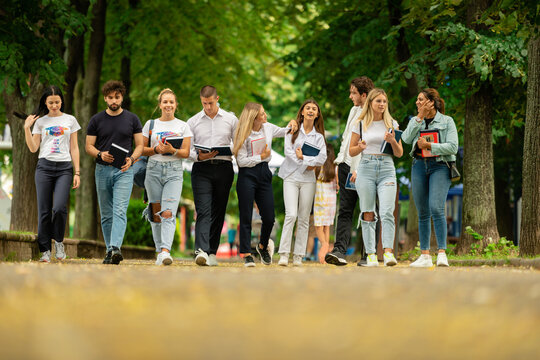 Big group of students. Large group of university students. College students walking. Students walking one next to each other. Students discussing while walking outdoors.