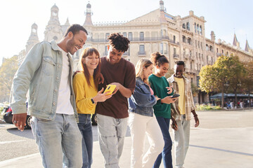 Group of smiling multiracial young people using cell phones. Cheerful students strolling around looking at technological devices. Happy fellow university students on study trip in European city. 