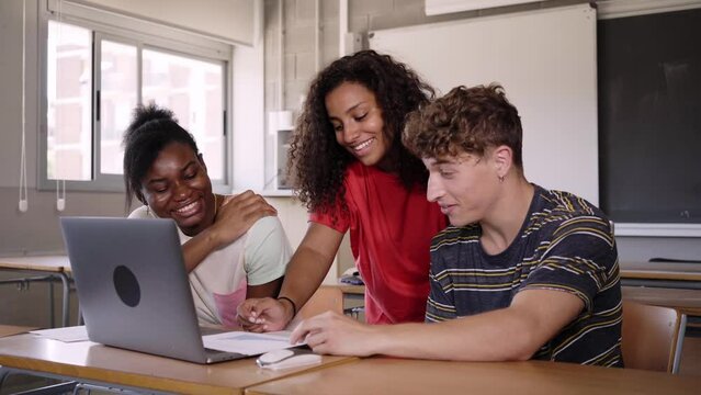Group of cheerful young multiracial students using laptop computer talking about final year project in university classroom. Education concept. Generation Z people and final exams.