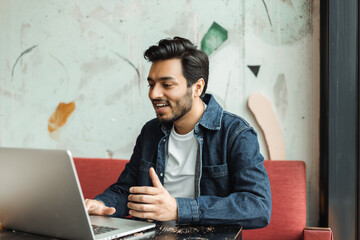 Handsome smiling Indian man, freelancer, programmer using laptop computer - obrazy, fototapety, plakaty