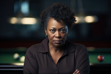 A middleaged African American female billiard player standing still her expression clearly visible against a soft background of billiard cues and table.