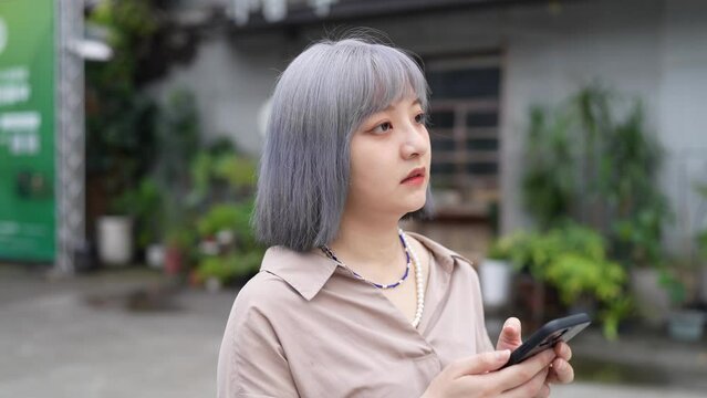 台湾台北の大通りでスマートフォンを操作しながらタクシーを待つ女性 A woman waits for a cab on a main street in Taipei, Taiwan, while operating a smartphone.