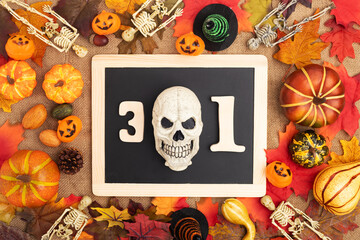 Number 31 in a black frame with a skull. Flat lay of skeletons, pumpkins and autumn foliage. Halloween holiday. View from above.