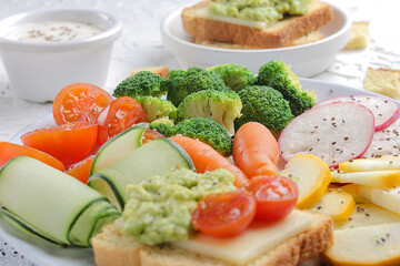 Antioxidant vegetable salad served on a white plate with guacamole and cheese spread on toast accompanied by greek yogurt and chia seeds.