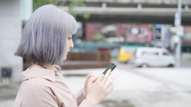 台湾台北の大通りでスマートフォンを操作しながらタクシーを待つ女性 A woman waits for a cab on a main street in Taipei, Taiwan, while operating a smartphone.