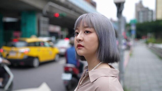 台湾台北の大通りでスマートフォンを操作しながらタクシーを待つ女性 A woman waits for a cab on a main street in Taipei, Taiwan, while operating a smartphone.