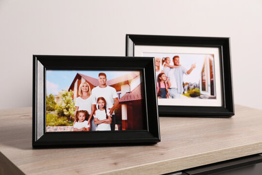 Frames with family photos on wooden table near white wall