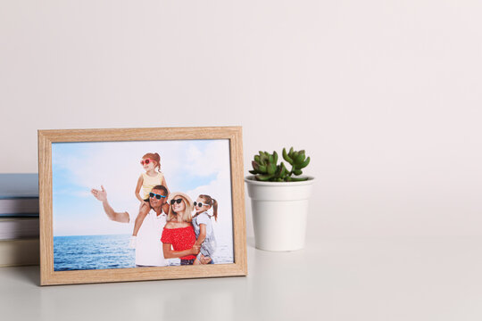 Frame with family photo and green houseplant on white table, space for text