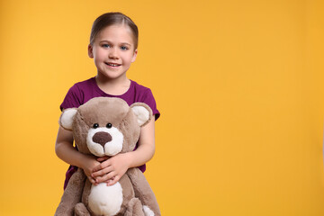 Cute girl with teddy bear on orange background, space for text