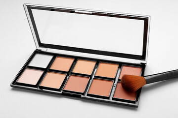 Colorful contouring palette with brush on light grey background, closeup. Professional cosmetic product