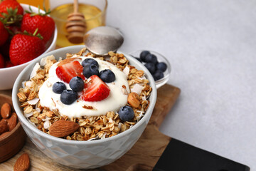 Tasty granola, yogurt and fresh berries in bowl on light table, closeup with space for text. Healthy breakfast