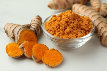Aromatic turmeric powder and raw roots on white table, closeup