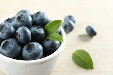 Bowl of fresh tasty blueberries with leaves on table, closeup. Space for text