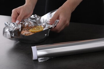 Aluminum foil and woman with tasty salmon at grey textured table, closeup - obrazy, fototapety, plakaty