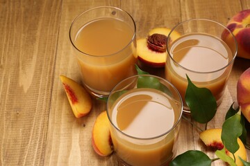 Glasses of peach juice, fresh fruits and leaves on wooden table