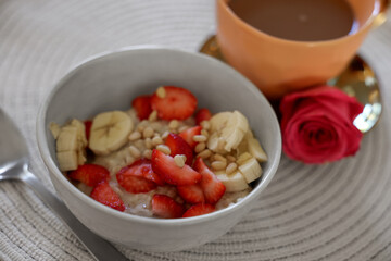 Delicious oatmeal with banana, strawberries, nuts and cup of hot drink on table, closeup