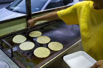 Cocinera calentando tortillas de maíz en un comal caliente. carrito de comida rápida callejera en...