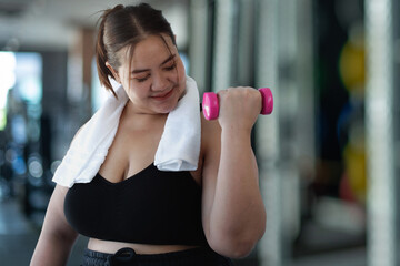 Happy overweight woman doing exercise with dumbbells at fitness gym, wearing sports wear