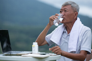 Asian old man sat in the atmosphere of the mountain view, drinking clean water after taking pills,...