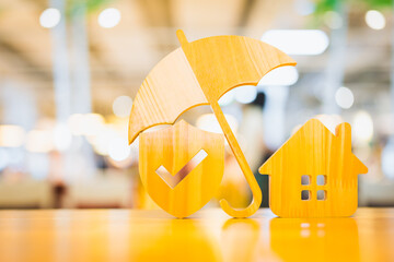 Model of umbrella and Shield protect icon with house on wooden table concept of the system of insurance savings and Housing insurance against impending loss and fire, building fire insurance concepts.