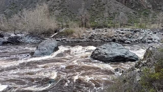 Huge stones in the bed of a small turbulent river flowing along the bottom of the canyon on a cloudy spring day. Chulyshman river, Altai, Sibir, Russia.