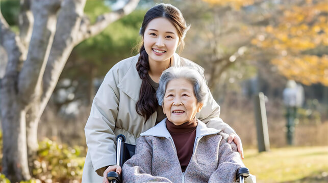 公園で車椅子に乗って散歩するアジア人の高齢者女性と介護士・家族
