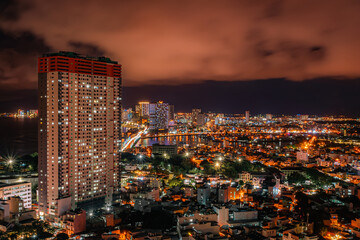 Nha Trang from the drone in the evening. In the background there is a skyscraper and many illuminated buildings. Orange clouds in the sky. Vietnam