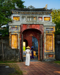 One of the colorful gates in the citadel of Hue. In the photo, two women standing backwards in the gate in traditional Vietnamese clothing. Vietnam.