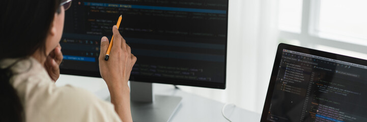 Developer programmer holds pencil and checking code on monitor while programming to developing web