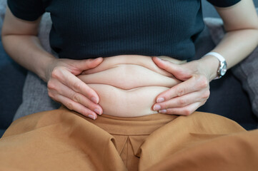 Cropped shot of woman touching and squeezing her fat belly.